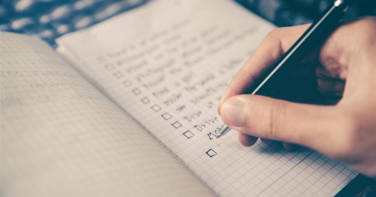 A hand with a pen ticking items off a checklist in a notebook, box by box